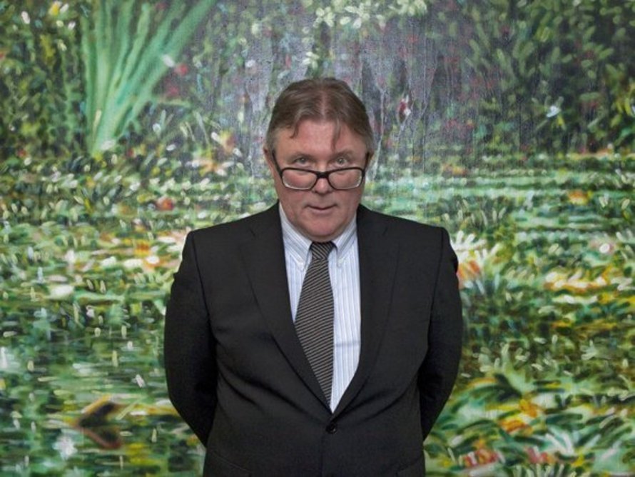 Künstler im dunklen Anzug mit Brille und Krawatte steht vor einem großformatigen Gemälde mit grüner Dschungellandschaft.